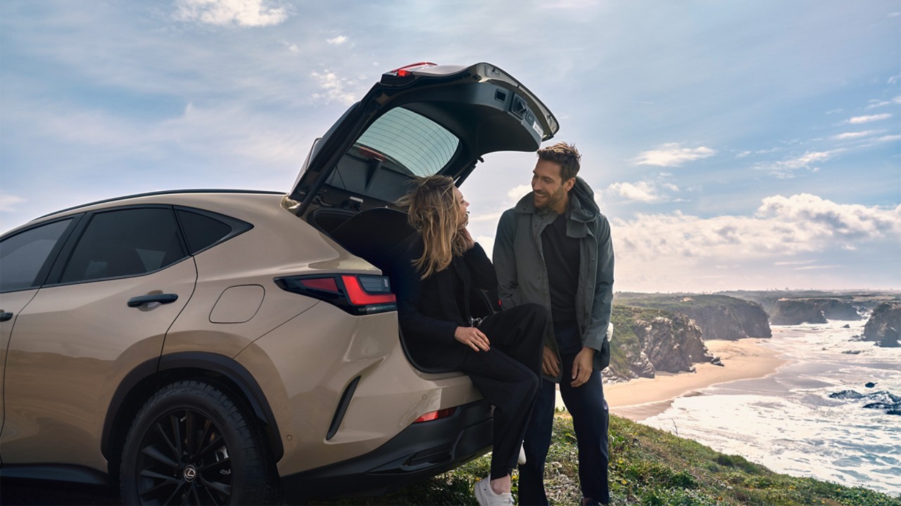 Two people stood behind a parked Lexus NX on a coastline